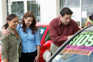 Parents looking at car on forecourt with daughter, smiling